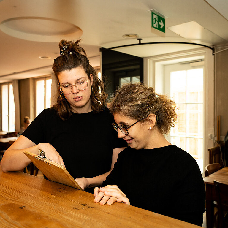 Eine Sozialpädagogin im Coaching mit einer Person mit Beeinträchtigung im Service. 